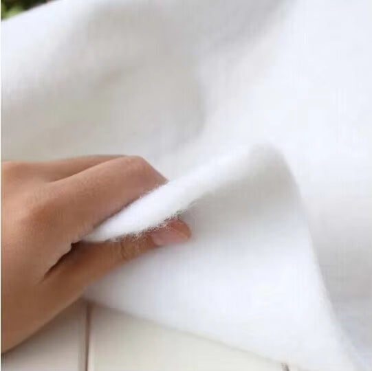 A hand holds a piece of white, fluffy material—a blend of cotton and polyester wadding—over a light background, showcasing the softness ideal for quilting and upholstery projects.