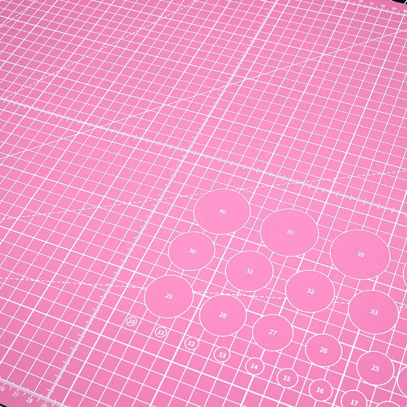 The A3 Double-Sided Self Healing Cutting Mat, in pink and high-quality PVC, features white grid lines, numbered circles, and measurement markings on a non-slip surface for precision and stability.