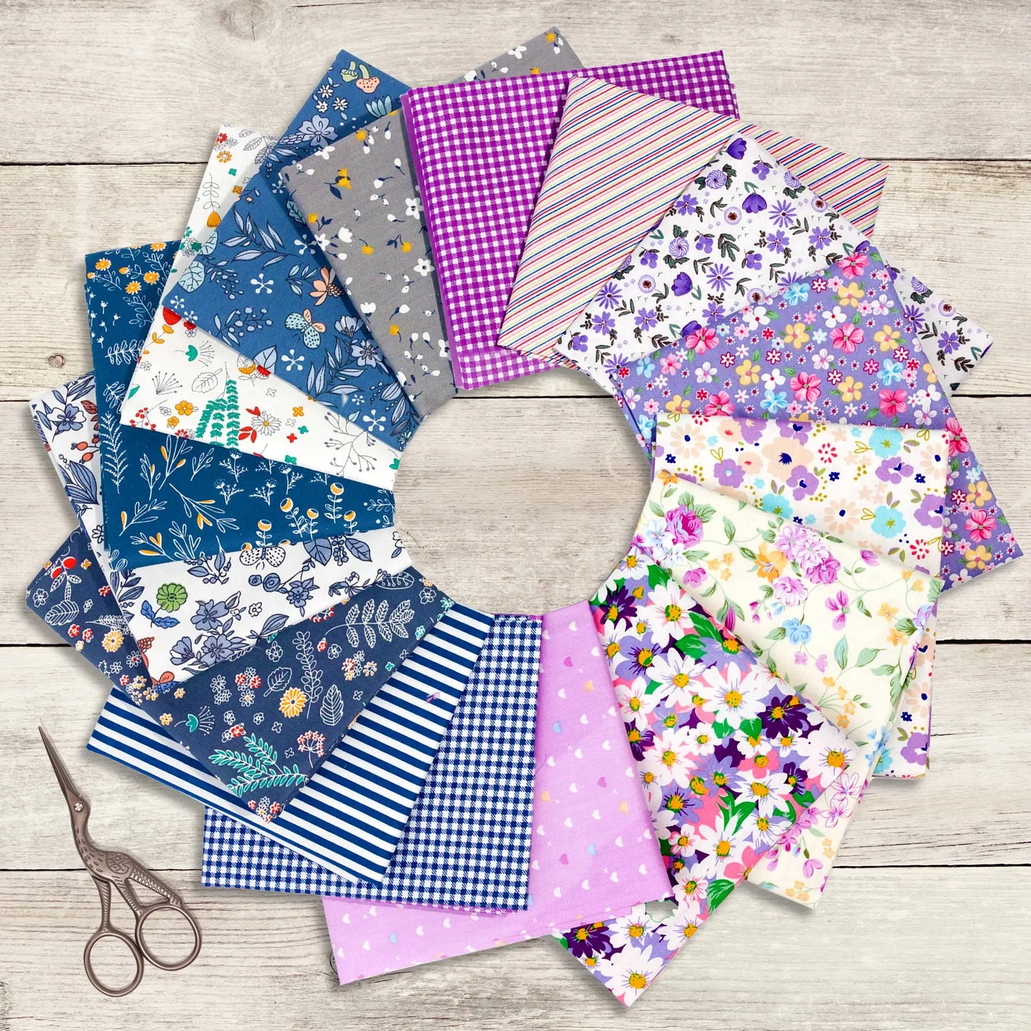 Assorted colorful fabric pieces laid out in a circular pattern with scissors on a wooden surface.