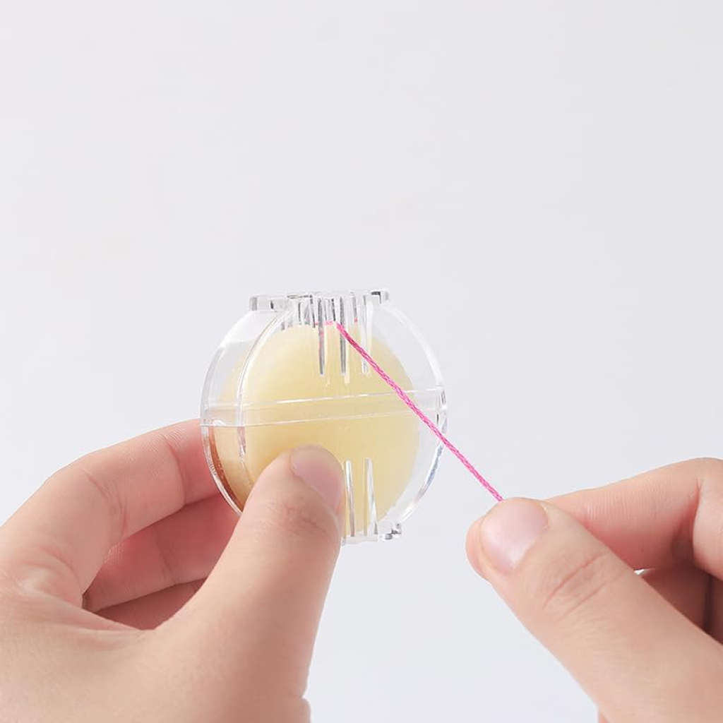 Hands pull pink thread from a dispenser holding Sewing Beeswax, likely to reduce breakage.