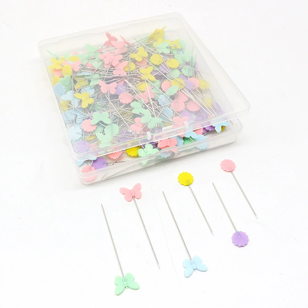 The Quilting Pins (200pcs) set includes pastel butterfly and flower heads, plus rust-resistant pins on a white surface; they provide exceptional holding power for sewing projects.
