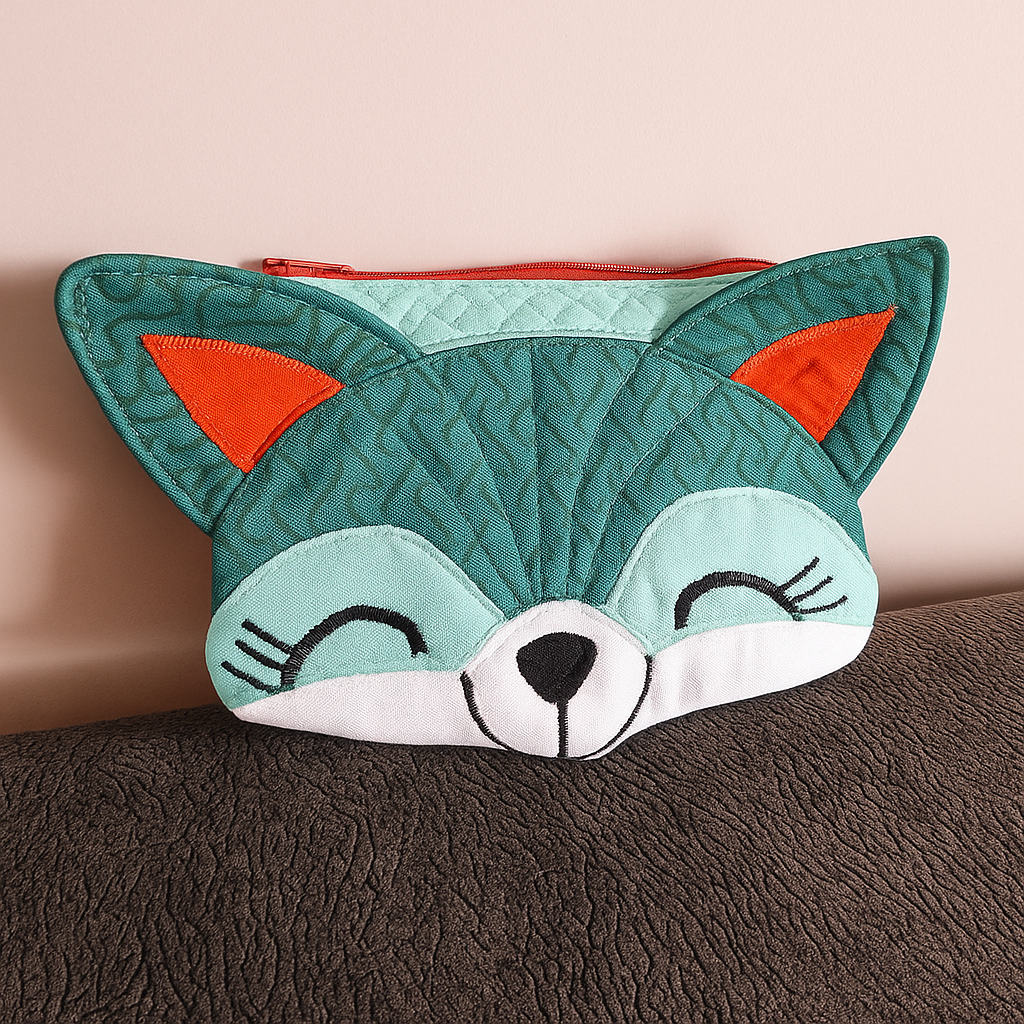 The Freddie Fox Purse Downloadable PDF Quilt Pattern lets you create a whimsical fabric pouch shaped like a fox's face, featuring teal and orange ears, a red zipper, and black embroidered features.