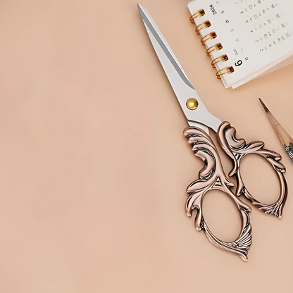 Embroidery Scissors, a pencil, and a small spiral-bound calendar are arranged on a beige surface, making these tools ideal quilting and crafting essentials.