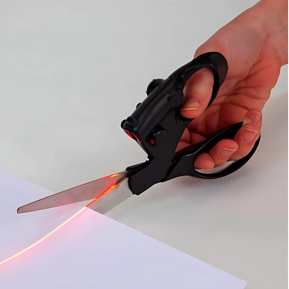 Laser-guided craft scissors projecting a red reference line on white paper