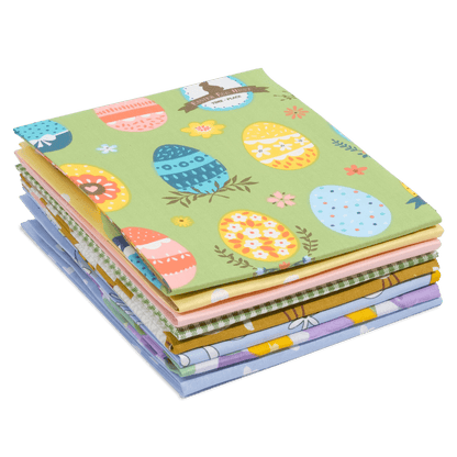 A stack of folded fabric squares from the Easter Bundle showcases various colorful patterns and designs, including Easter eggs and flowers.