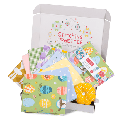 Unbox the Easter Bundle featuring vibrant fabric squares with Easter themes and a small, yellow pincushion. Branded as "Stitching Together.