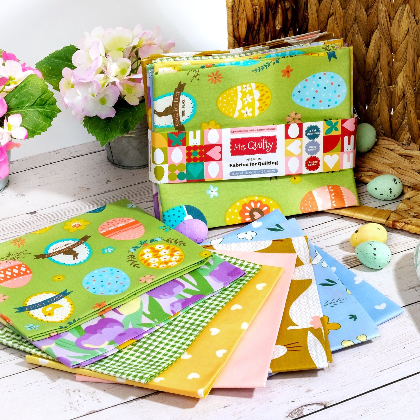 The Easter Bundle boasts colorful quilting fabrics with egg and flower designs, artfully displayed on a white wood surface alongside small decorative eggs and pink hydrangeas.