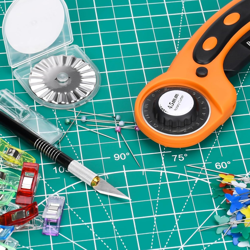 The 97-Piece Quilting Kit: Perfect for Beginners includes essentials like a rotary cutter, craft knife, pins, clips, and wavy blade—all arranged on a green cutting mat with measurement grids.