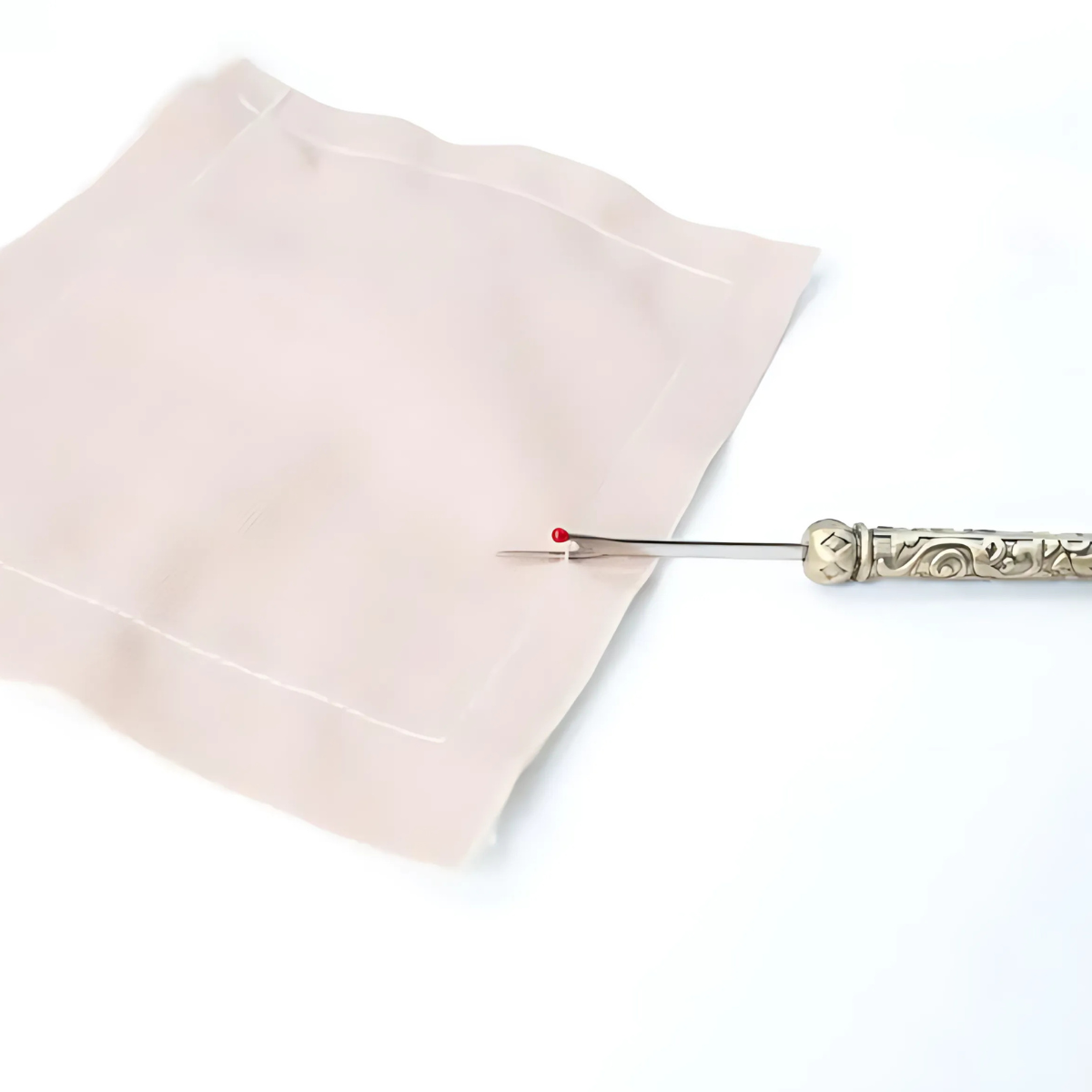 The Vintage Seam Ripper Set, featuring an ornate ergonomic design with vintage charm, is displayed beside a square piece of light pink fabric on a white background.