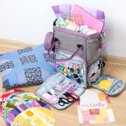 A Wooden Sewing Box with Handle (Images54) filled with quilting supplies like fabric, threads, scissors, and pincushions sits open next to a patchwork quilt, colorful fabric circles, and a "Mrs. Quilty" booklet.
