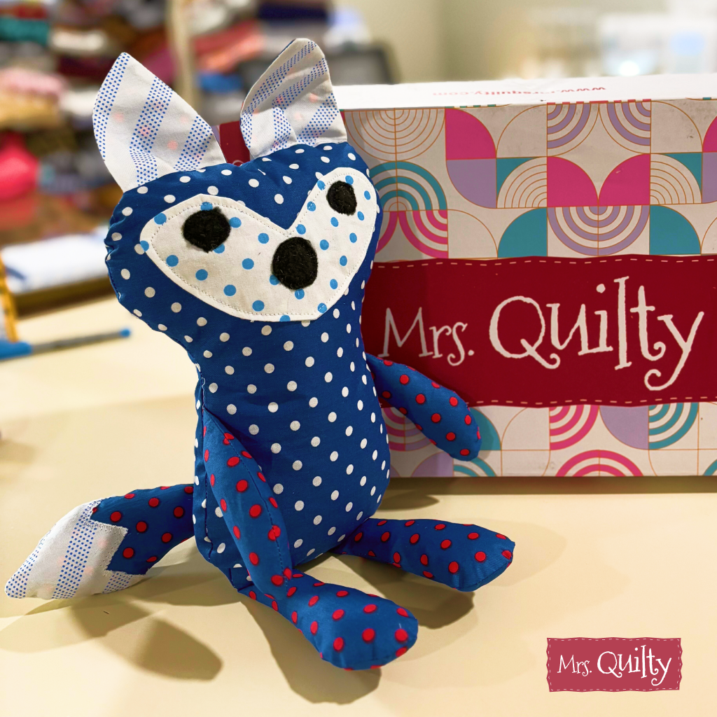 A colorful box labeled "Mrs. Quilty" sits beside a sample made from the Finley the Fox Downloadable PDF Quilt Pattern in a craft store display.