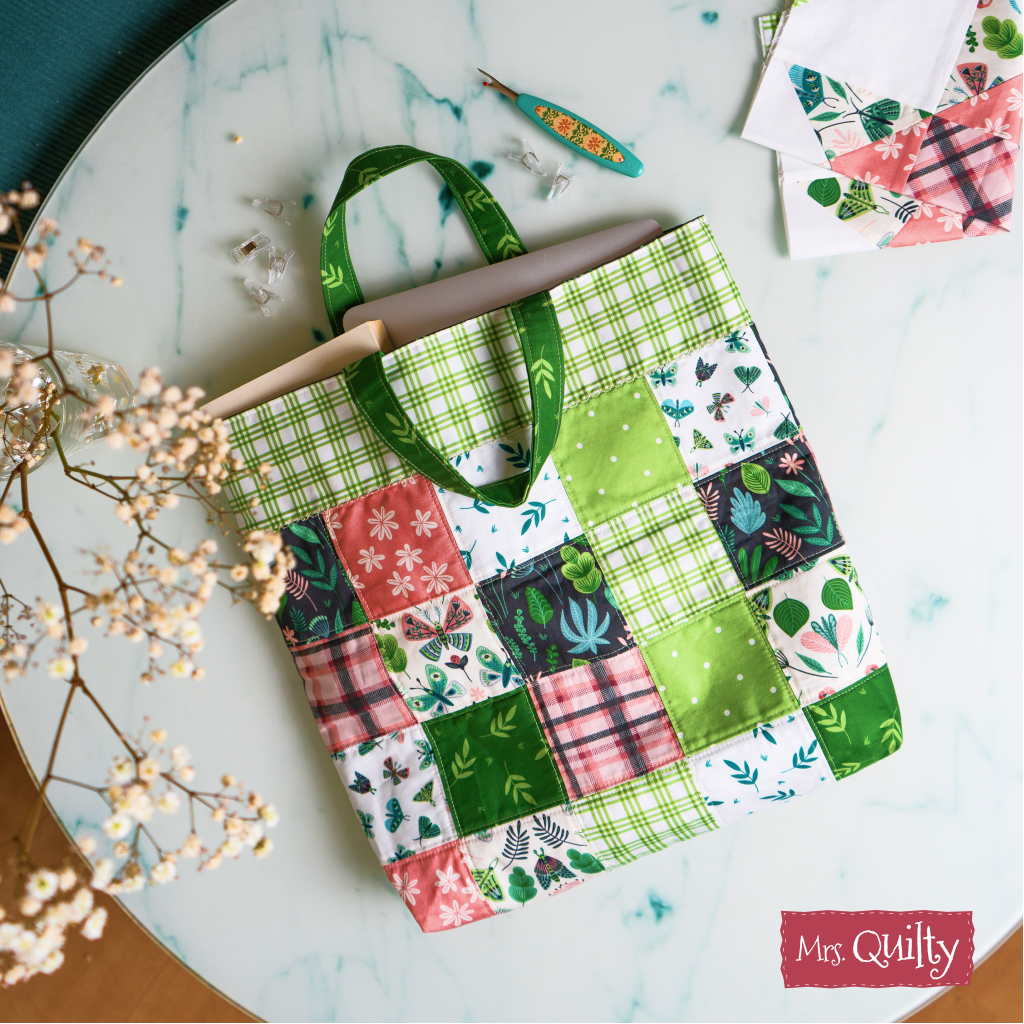Perfect for quilting enthusiasts, the Tote Bag Downloadable PDF Quilt Pattern features instructions for a patchwork bag with green, pink, and patterned squares. Sturdy handles and room for papers make it both stylish and practical.