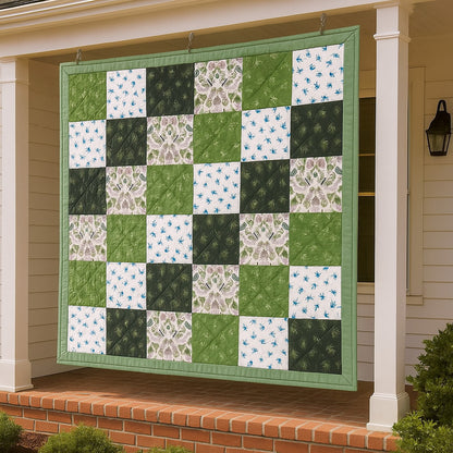 A variety of quilt patterns from the Bundle of 14 Quilt Patterns, including floral designs, are featured on a green and white patchwork quilt hanging on a porch before a white house with a brick base.