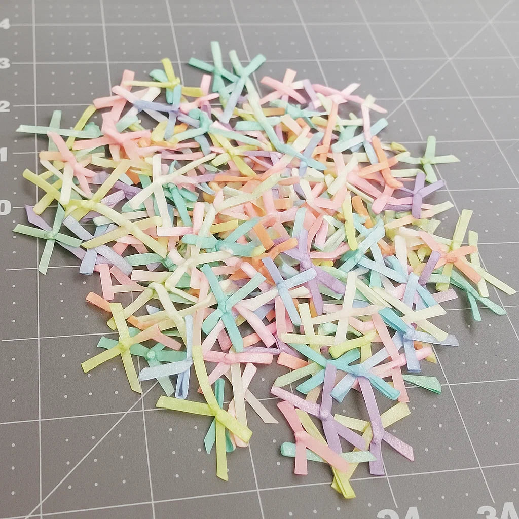 A set of small, pastel-colored satin ribbons from the Pastel Satin Ribbon Set is scattered on a gray cutting mat with measurement lines.