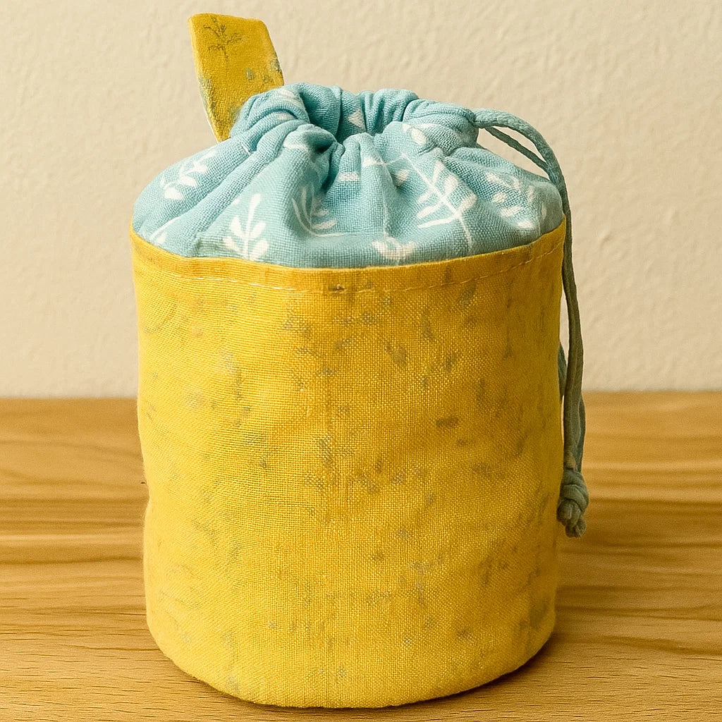 A yellow and blue fabric pouch with a leaf-patterned blue section rests on wood—crafted using the Dog Treat Bag Downloadable PDF Quilt Pattern, ideal for pet lovers or as a fun sewing project.