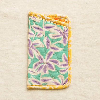 The Quilted Glasses Sleeve Downloadable PDF Quilt Pattern features a floral design in green, purple, and yellow—perfect for fans of beginner quilting patterns. Displayed on a neutral beige background.