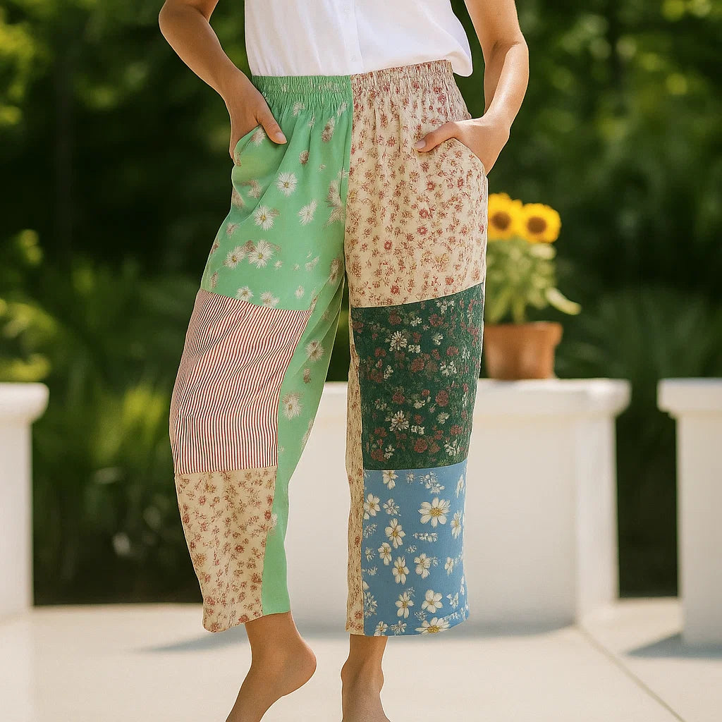 A person stands barefoot outdoors with hands in pockets, wearing pants made using the Patchwork Pants Downloadable PDF Quilt Pattern, with sunflowers and greenery in the background.