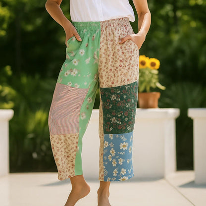A person stands barefoot outdoors with hands in pockets, wearing pants made using the Patchwork Pants Downloadable PDF Quilt Pattern, with sunflowers and greenery in the background.