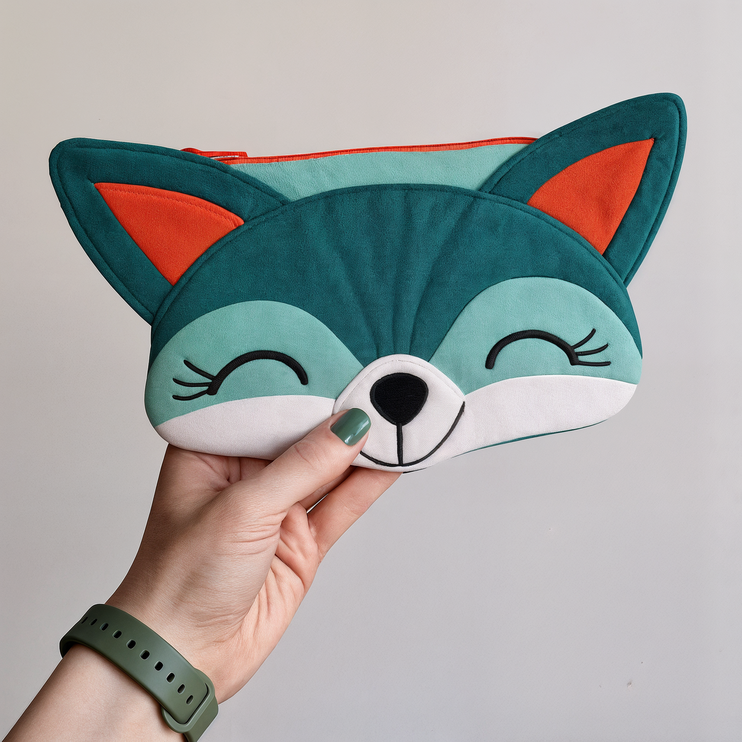 A hand holds the Freddie Fox Purse Downloadable PDF Quilt Pattern, a whimsical accessory in teal, white, and orange with a smiling face and closed eyes.