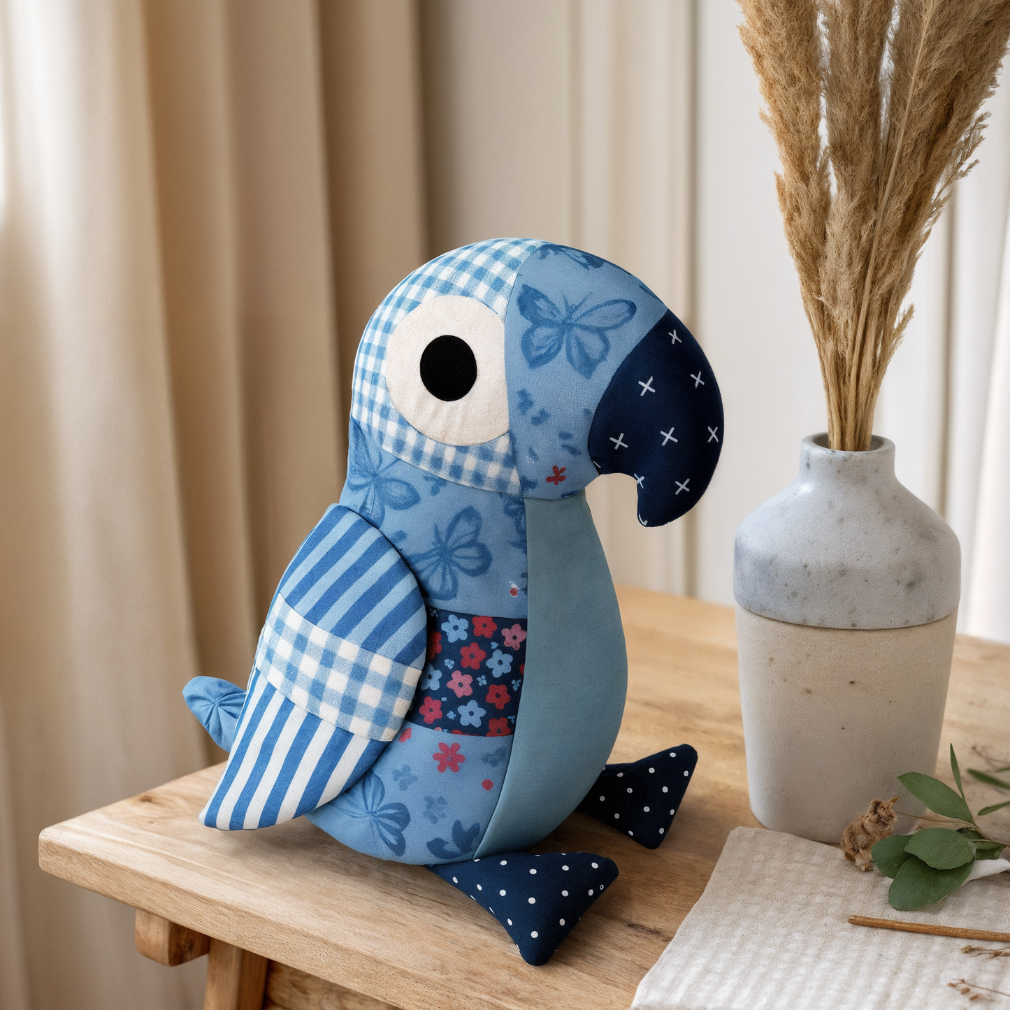 Blue patchwork parrot toy on a wooden surface with a vase and plant in the background