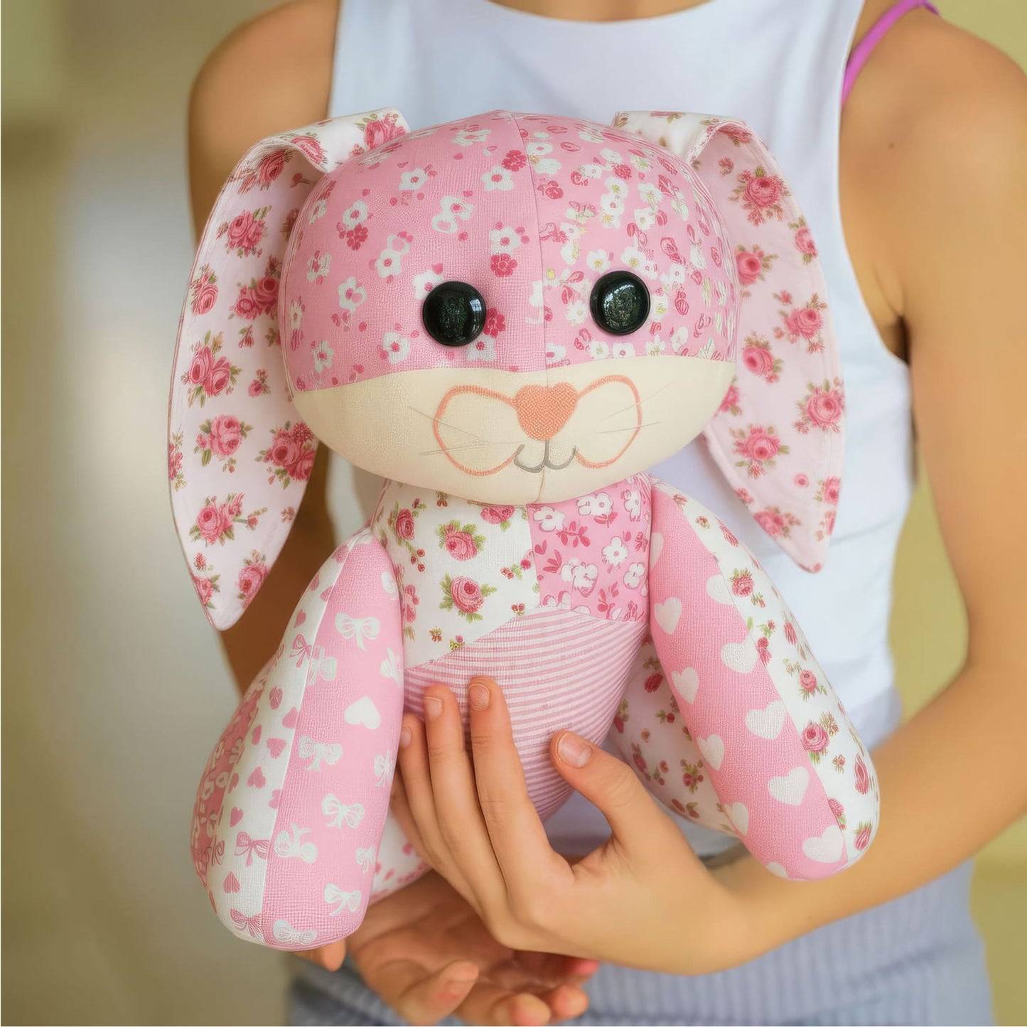 Someone in a white tank top holds a pink, floral-patterned bunny from the Mrs. Quilty Plushies – Bundle of 14 Quilted Patterns, highlighting the charm of handmade stuffed animals with button eyes and a heart-shaped nose.