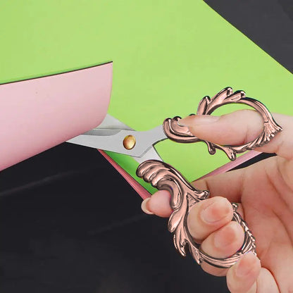 A hand uses Embroidery Scissors to cut pink paper layered over green, evoking a vintage quilting craft.